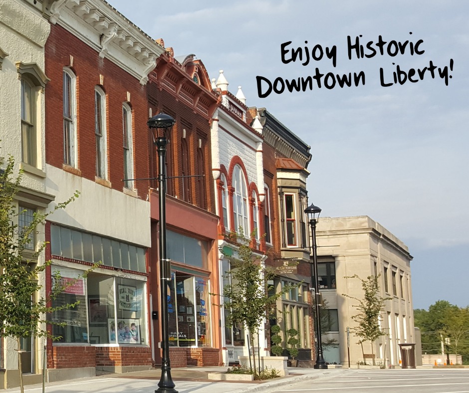 Red brick Victorian storefronts along the Liberty Square in downtown Liberty, Missouri, with cast iron street lamps and young trees on the sidewalk